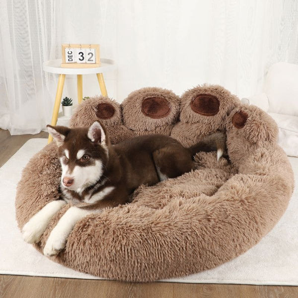 Coussin pour chien en forme de patte marron foncé avec un husky allongé dessus